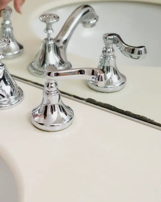 Hand adjusting a chrome faucet in a bright bathroom
