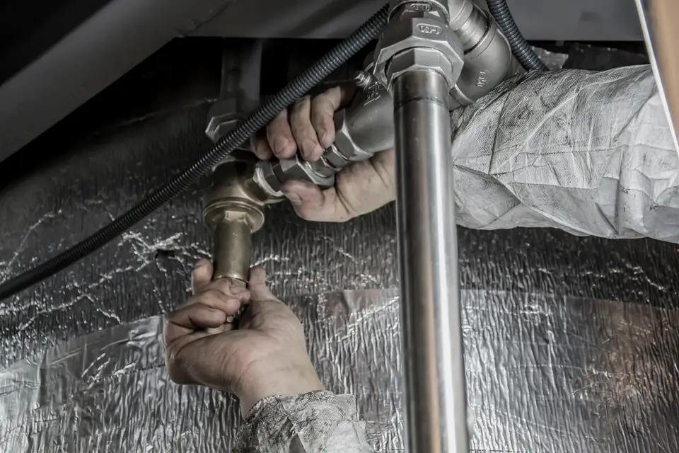 Plumber's hands working on insulated pipe under a cabinet