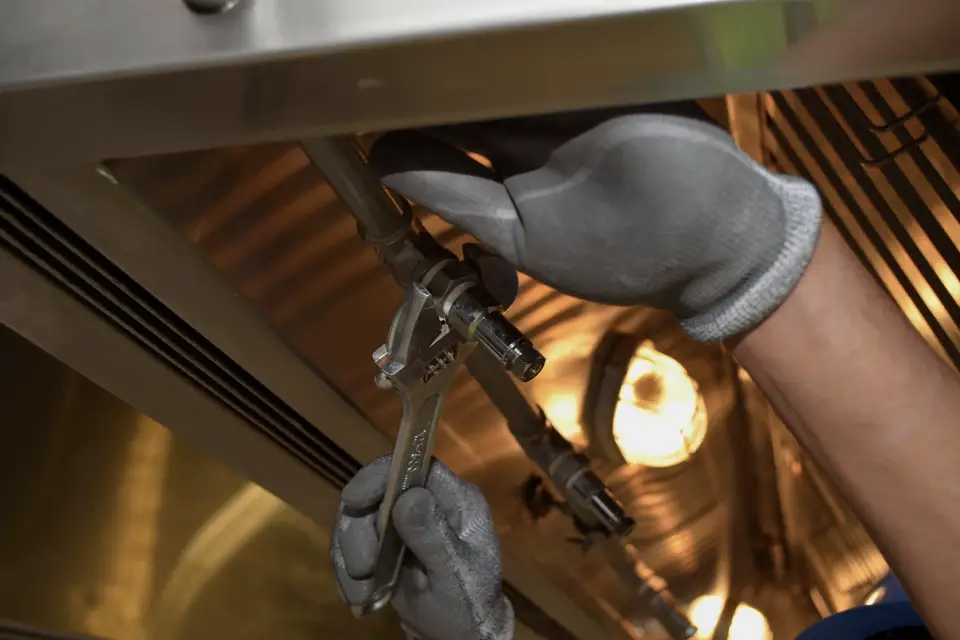 Gloved hands tightening a fitting overhead