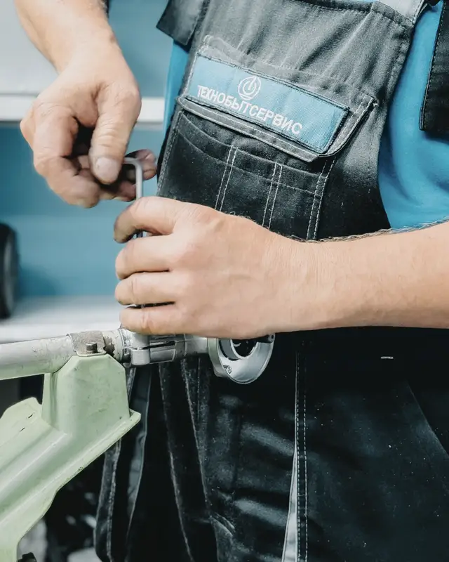 Plumber in a blue uniform working on a pipe with a wrench